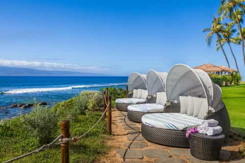 Luxury oceanfront cabana beds with canopies overlooking waves and palm trees