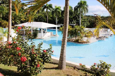 Tropical resort lazy river pool with white cabanas, palm trees, and lush green landscaping