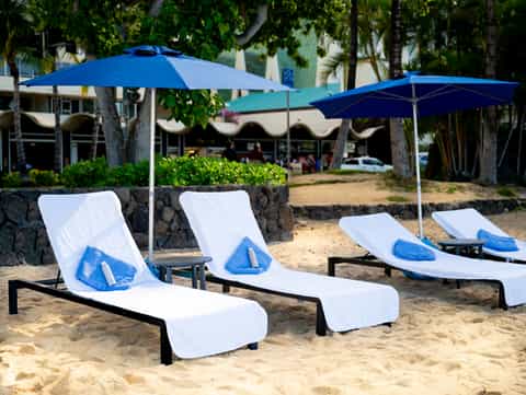 Sandy beach lounge chairs with blue umbrellas and towels under palm trees