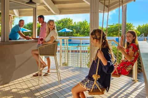 Family enjoying waterfront bar area with pool view and palm tree landscape