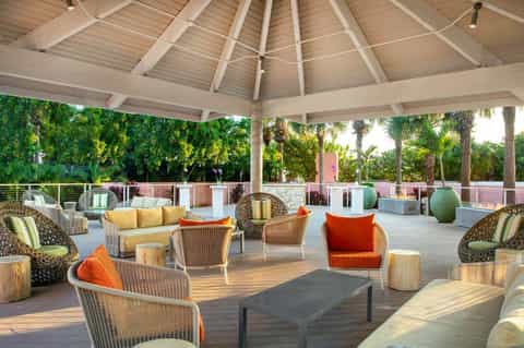 Modern covered pavilion with woven chairs and yellow cushions overlooking palm-lined landscape