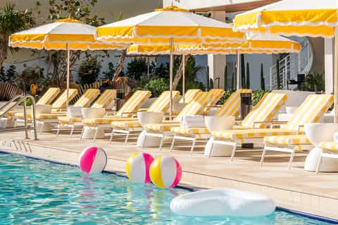 Resort pool deck with yellow and white striped loungers under matching umbrellas and colorful beach balls