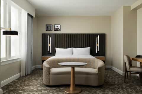 Modern hotel bedroom with black upholstered headboard and curved lounge seating