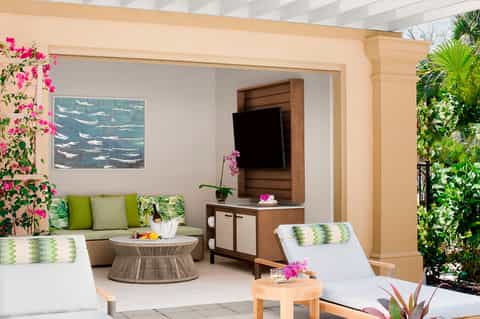 Tropical resort suite terrace with lounge chairs, living area, magenta flowers, and lush greenery