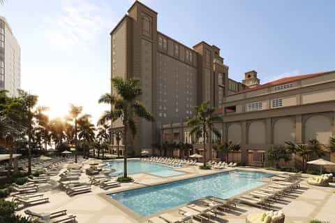 Grand resort courtyard with multiple pools, palm trees, and main building