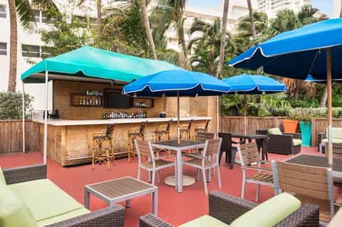 Beachside bar with turquoise umbrellas, wooden counter, bar seating, and tropical palm trees