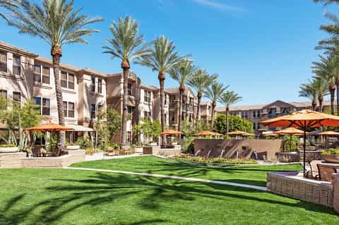 Resort courtyard with palm trees, green lawn, orange umbrellas, and apartment buildings