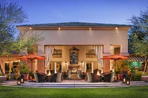 Evening resort patio with fireplace, rattan seating, orange umbrellas, and uplighting