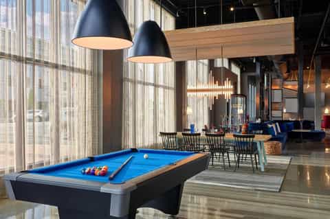 Contemporary lounge with pool table, pendant lights, blue accents, and floor-to-ceiling windows