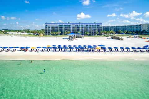 Beachfront resort building with blue umbrellas lining pristine sandy beach and clear turquoise Gulf waters.