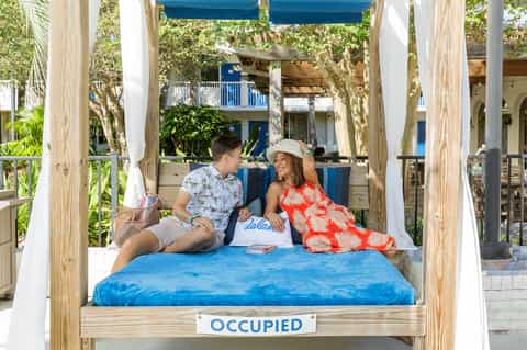 Couple sitting on a large blue daybed at a resort with tropical architecture and palm trees