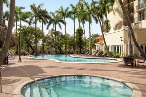 Resort pool surrounded by palm trees, lounge chairs, and Spanish-style architecture