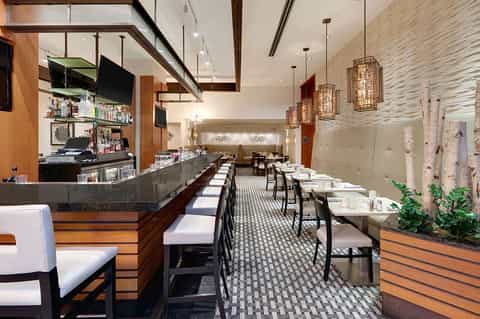 Contemporary hotel restaurant with bar counter, dining tables, and decorative pendant lights