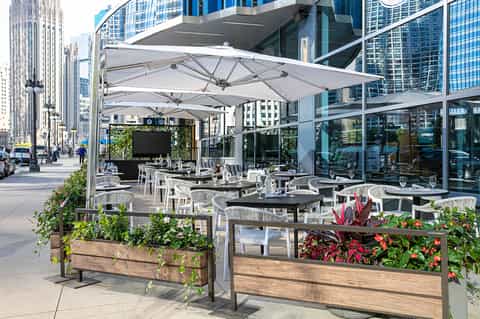 Urban rooftop dining patio with white umbrellas, planters, and city skyline views