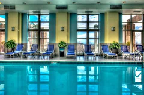 Indoor pool with blue loungers, large windows, yellow and turquoise walls, city view in background