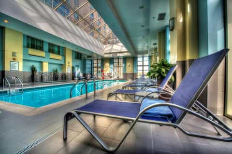 Indoor hotel pool with blue water, glass ceiling, lounge chairs, yellow and teal walls