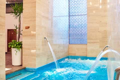 Modern indoor spa with blue tiled hot tub, geometric window patterns, and marble walls
