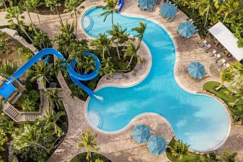 Overhead view of resort pool complex with water slides, umbrellas, and lush palm tree landscaping