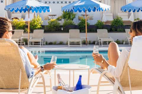 Women relaxing poolside with cocktails under blue and white umbrellas