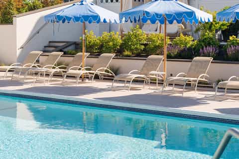 Resort pool with lounge chairs under blue and white striped umbrellas and landscaped gardens