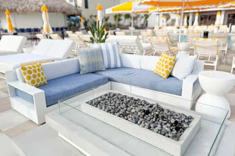 Beach club lounge with blue and white sectional, fire pit, yellow umbrellas, and ocean views