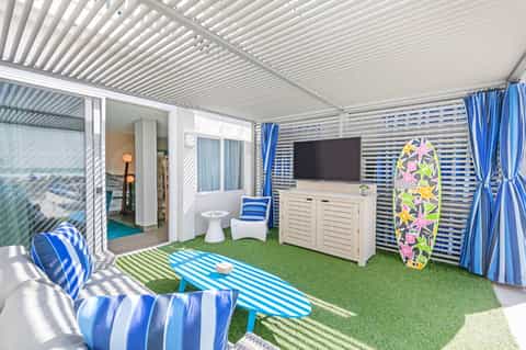 Covered beach cabana with striped blue and white decor, TV, green turf floor, and ocean access