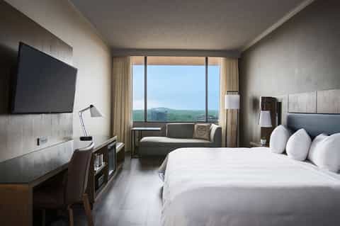 Contemporary hotel bedroom with king bed, flat-screen TV, and floor-to-ceiling window with mountain view