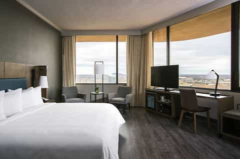 Hotel room with king bed, sitting area, and panoramic windows with city landscape view