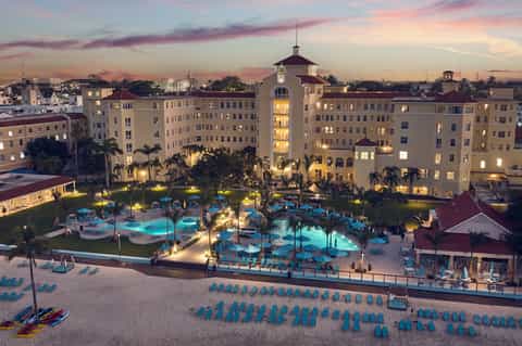 Illuminated resort pools and courtyard at twilight with palm trees and historic-style buildings