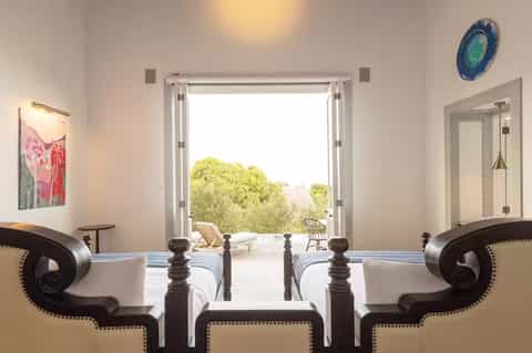 Luxury bedroom with twin beds, ocean view through open doors, and minimalist white décor