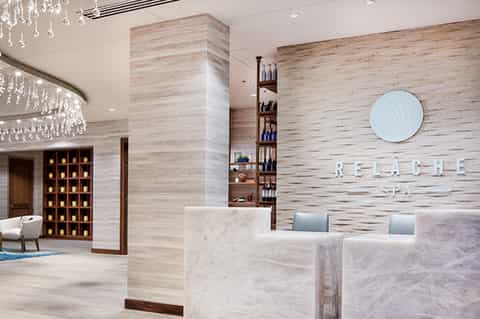 Modern spa reception area with light wood walls, crystal chandelier, and marble counters