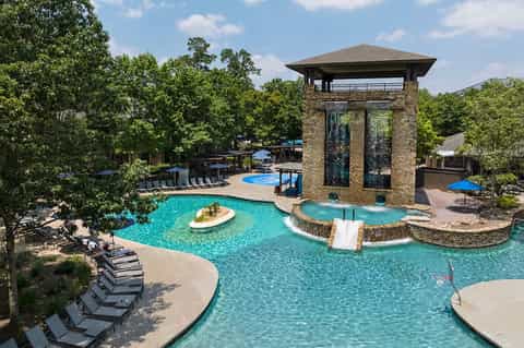 Luxury resort pool complex with turquoise water, floating island, stone tower structure, and surrounding lounge areas