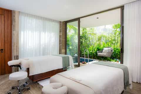 Spa treatment room with two massage beds overlooking tropical garden through large glass doors