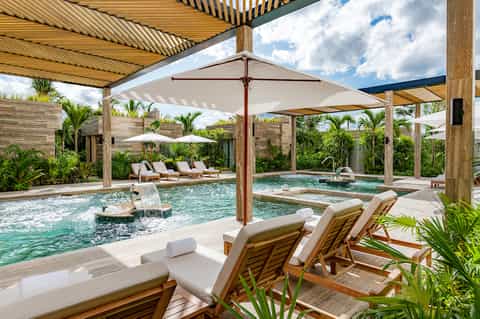 Tropical spa pool area with lounge chairs, umbrellas, wooden pavilion, and surrounding palm landscaping