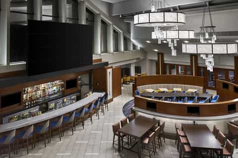Modern hotel bar and lounge with curved counter, crystal chandeliers, and seating area
