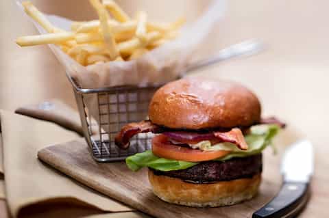 Gourmet burger with bacon and vegetables served with French fries in wire basket