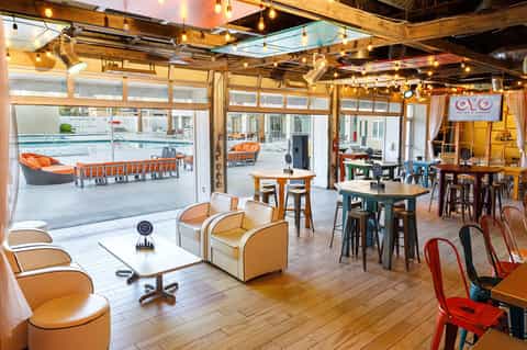 Casual resort pool bar and lounge with orange seating, glass doors, wooden ceiling, and pool views
