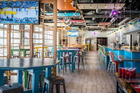 Colorful sports bar interior with multiple TVs, high-top tables, and pool tables