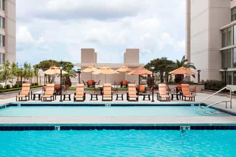 Resort pool deck with blue water, lounge chairs, orange umbrellas, and high-rise buildings in background