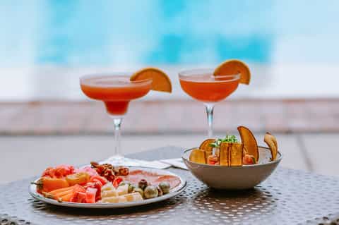 Cocktails and appetizers on table by pool overlooking beach and blue sky
