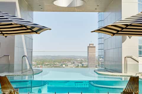 Indoor infinity pool with striped umbrellas overlooking city skyline and mountains