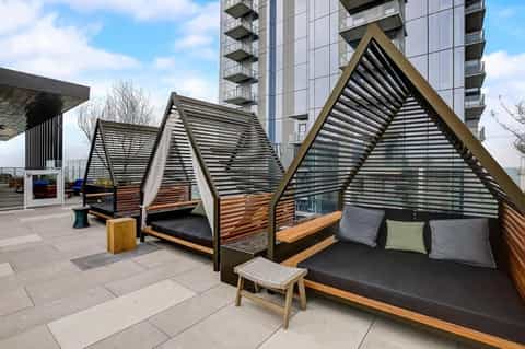 Modern rooftop lounge with geometric shade structures, wooden seating, and urban building backdrop