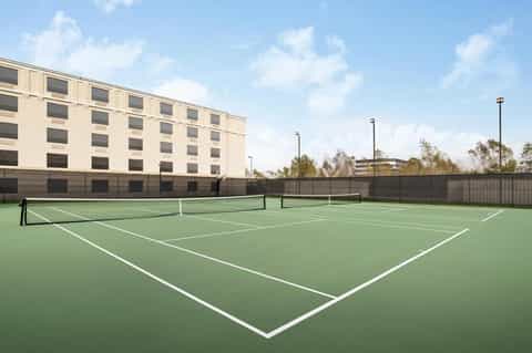Outdoor tennis courts with green playing surface adjacent to modern hotel building