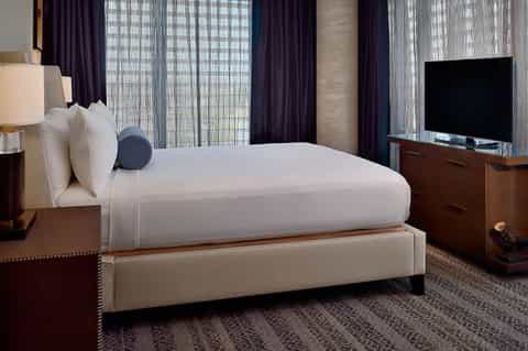 Modern hotel bedroom with king bed, dark curtains, and city view windows