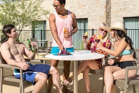 Group of guests enjoying drinks at outdoor patio table near stone building during daytime