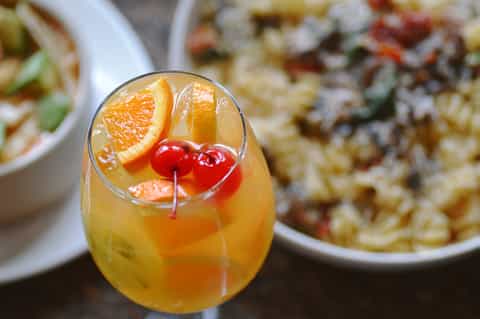 Golden cocktail with orange slice and maraschino cherries beside pasta dishes