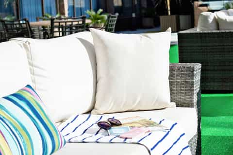 Outdoor lounge seating with white pillows, striped blanket, and colorful cushion on green artificial turf