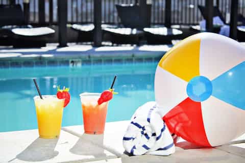 Poolside cocktails with beach ball and towel on deck chair by resort pool