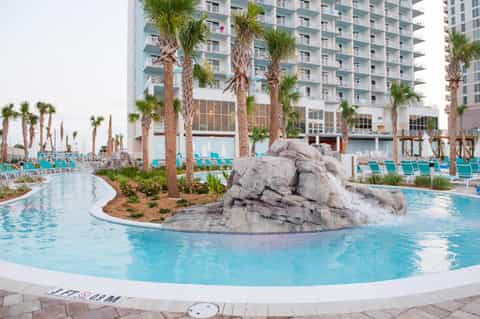 Lazy river pool with rock features, tall palm trees, and high-rise resort buildings in background