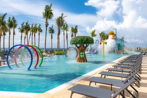 Family water park with colorful splash pad, palm trees, and lounge chairs